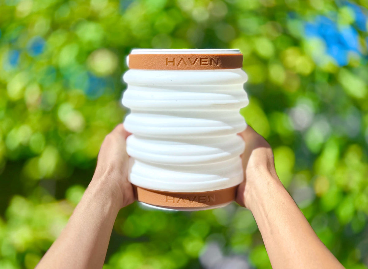 Collapsible solar lantern with 'Haven' branding on adjustable handles held by hands against a nature background.