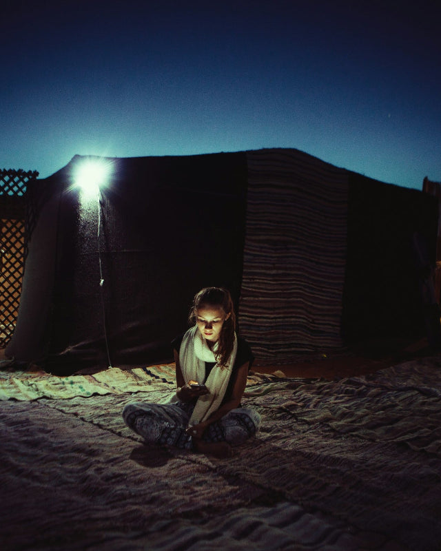 Young girl sitting in a dimly lit outdoor refugee tent setting with HAVEN solar portable lantern in the background.