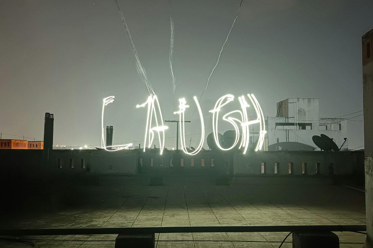 Portable solar lights creating light trails using slow shutter speeds that spell  'LAUGH' on a rooftop at night