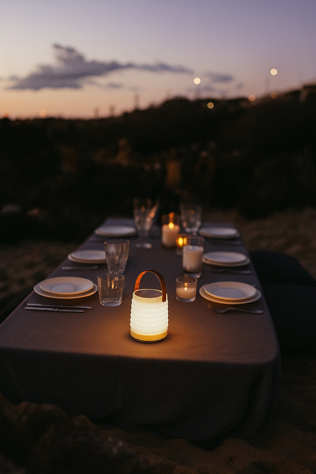 Dinner table set for an outdoor picnic on a beach at dusk with candles and a HAVEN solar portable lantern to set the mood.