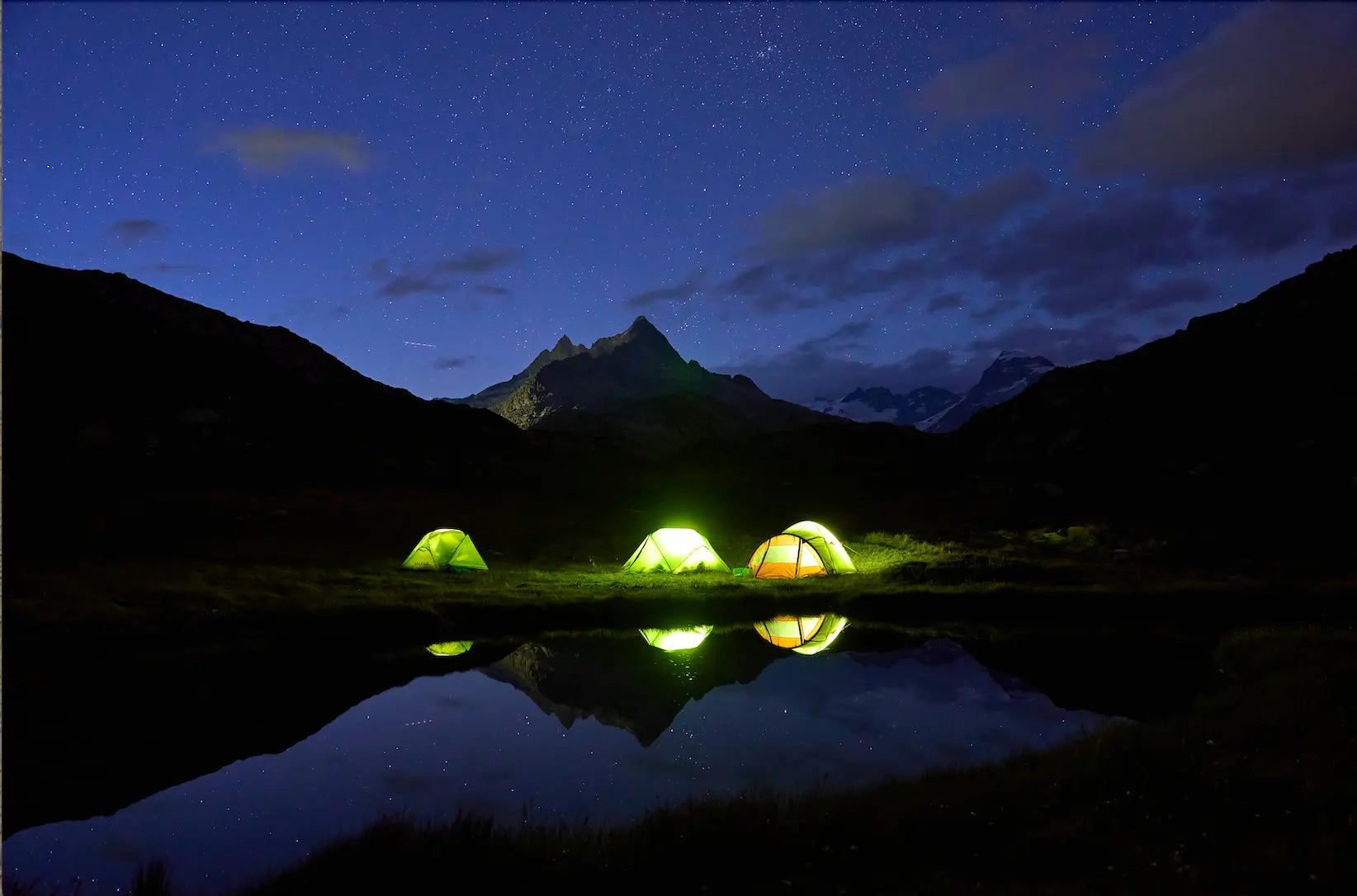 Three tents illuminated with HAVEN Lanterns in a mountainous area at night with stars in the sky.