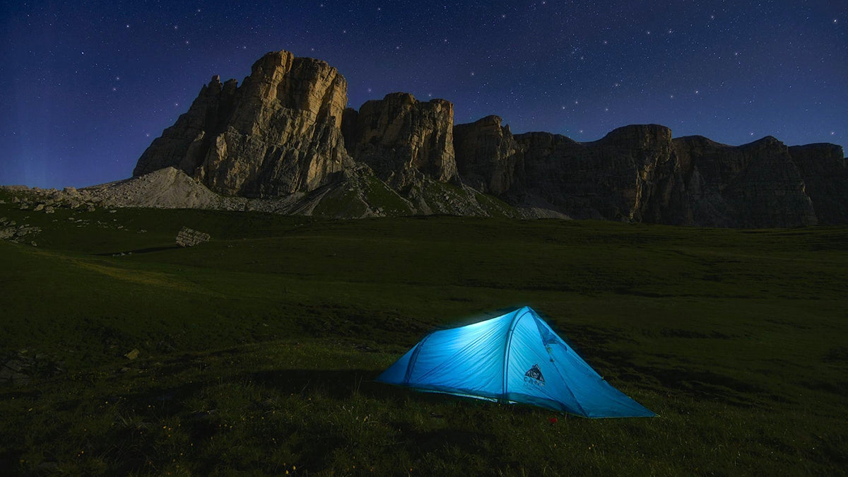 Blue camping tent lit up with a HAVEN solar portable lantern and power bank under a starry night sky with mountains in the background.