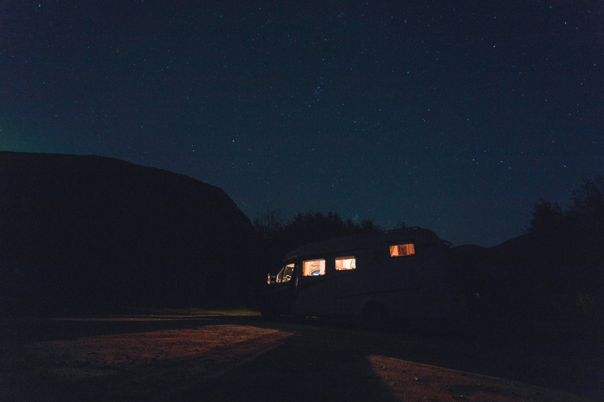 HAVEN portable solar lantern and power bank lighting up a RV camper in a campsite against a dark, starry night sky.