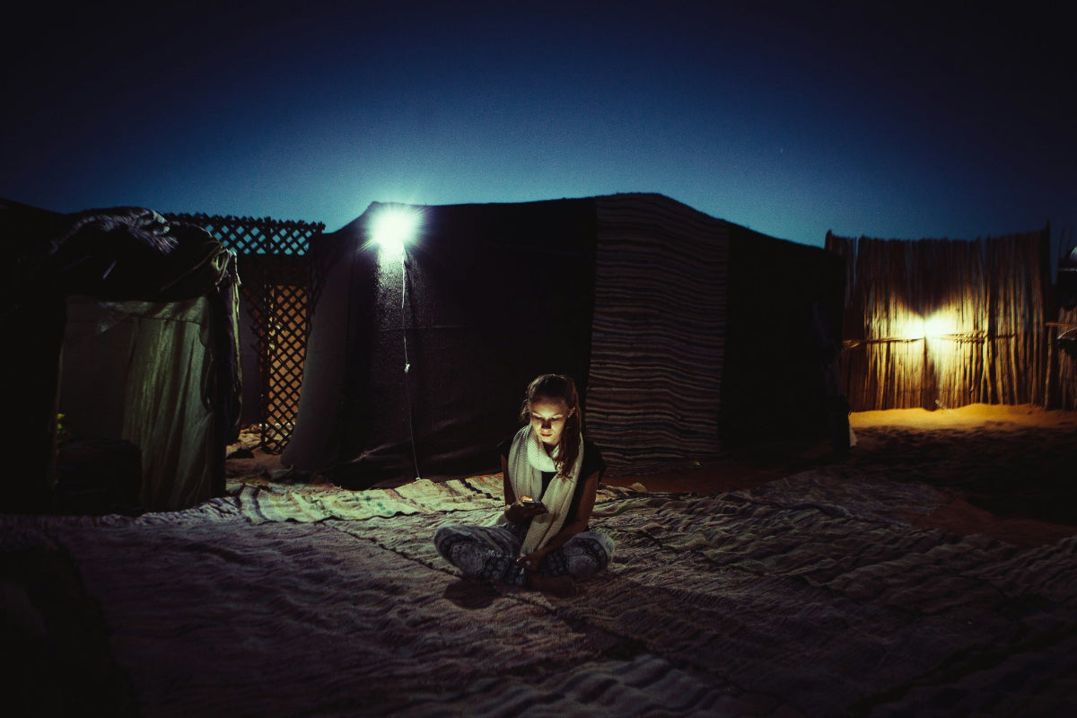 Young girl sitting in a dimly lit outdoor refugee tent setting with HAVEN solar portable lantern in the background.