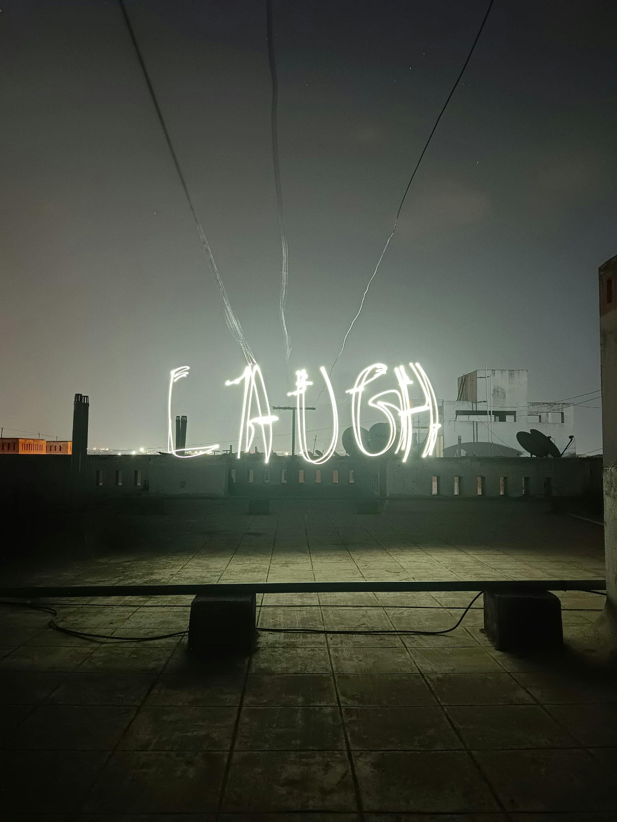Portable solar lights creating light trails using slow shutter speeds that spell  'LAUGH' on a rooftop at night
