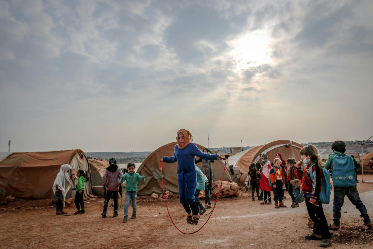 Children playing in a refugee camp with tents and a cloudy sky.
