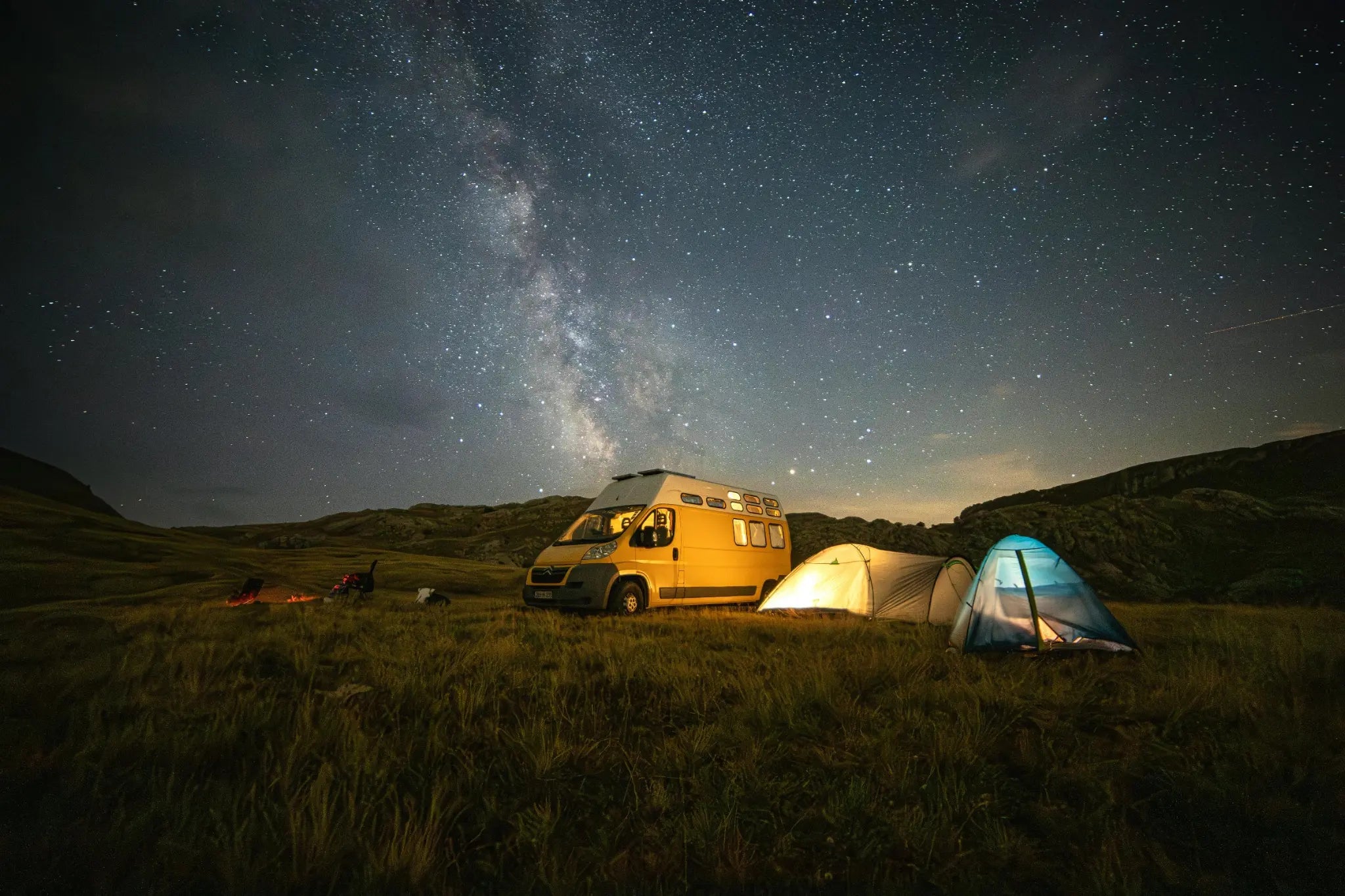 Yellow camper van and tents illuminated with HAVEN Lanterns under a starry night sky