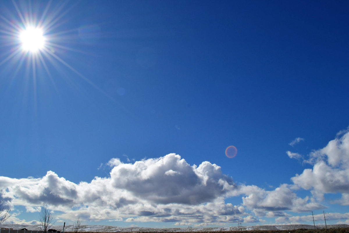 Clear blue sky with white clouds and a bright sun illuminating the power of solar energy.