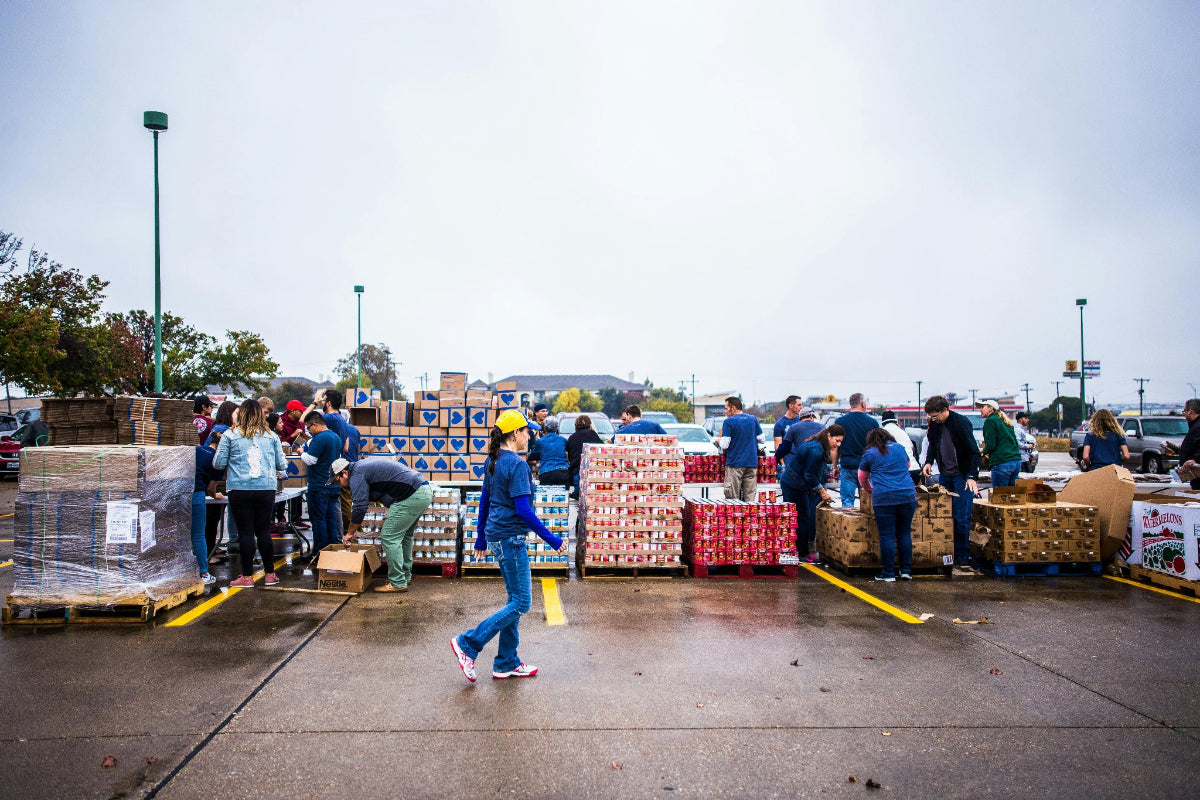 Corporate volunteers sorting and organizing boxes of disaster relief supplies in a community parking lot.