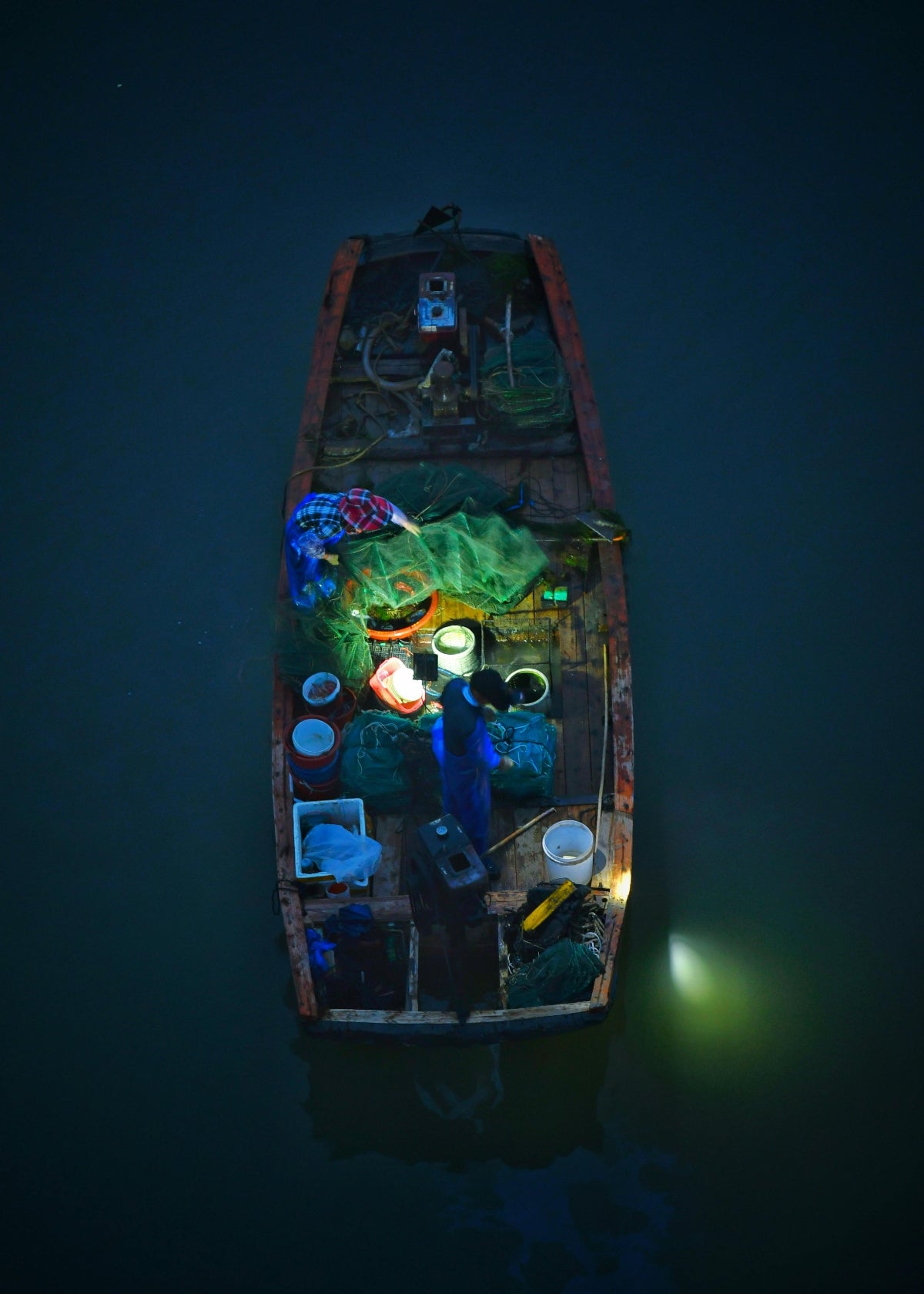 Small boat with fishing equipment at night on a dark water surface lit up by a HAVEN portable solar lantern.