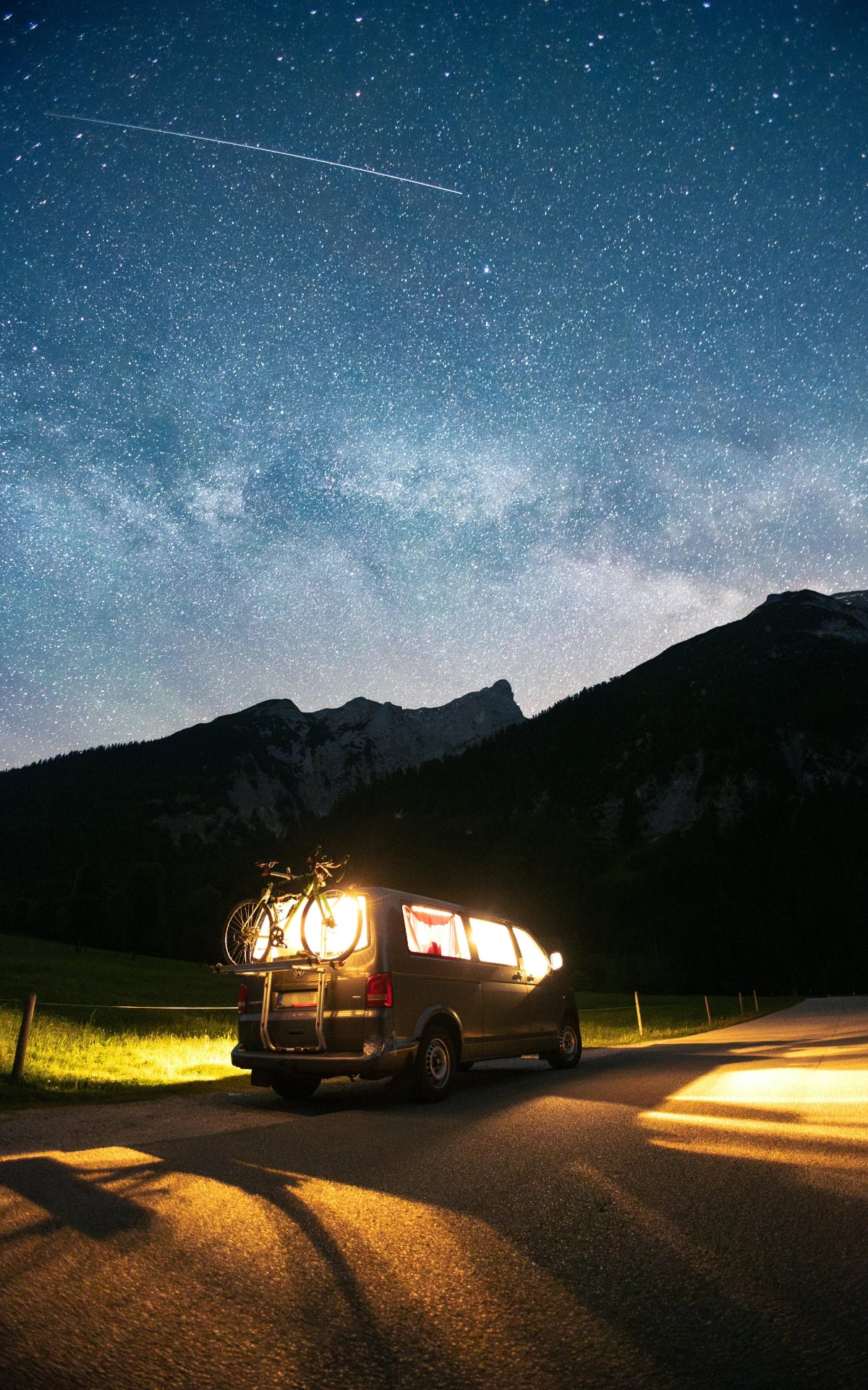 Camper van with bicycle lit up with HAVEN solar portable lantern under a starry sky with mountains in the background