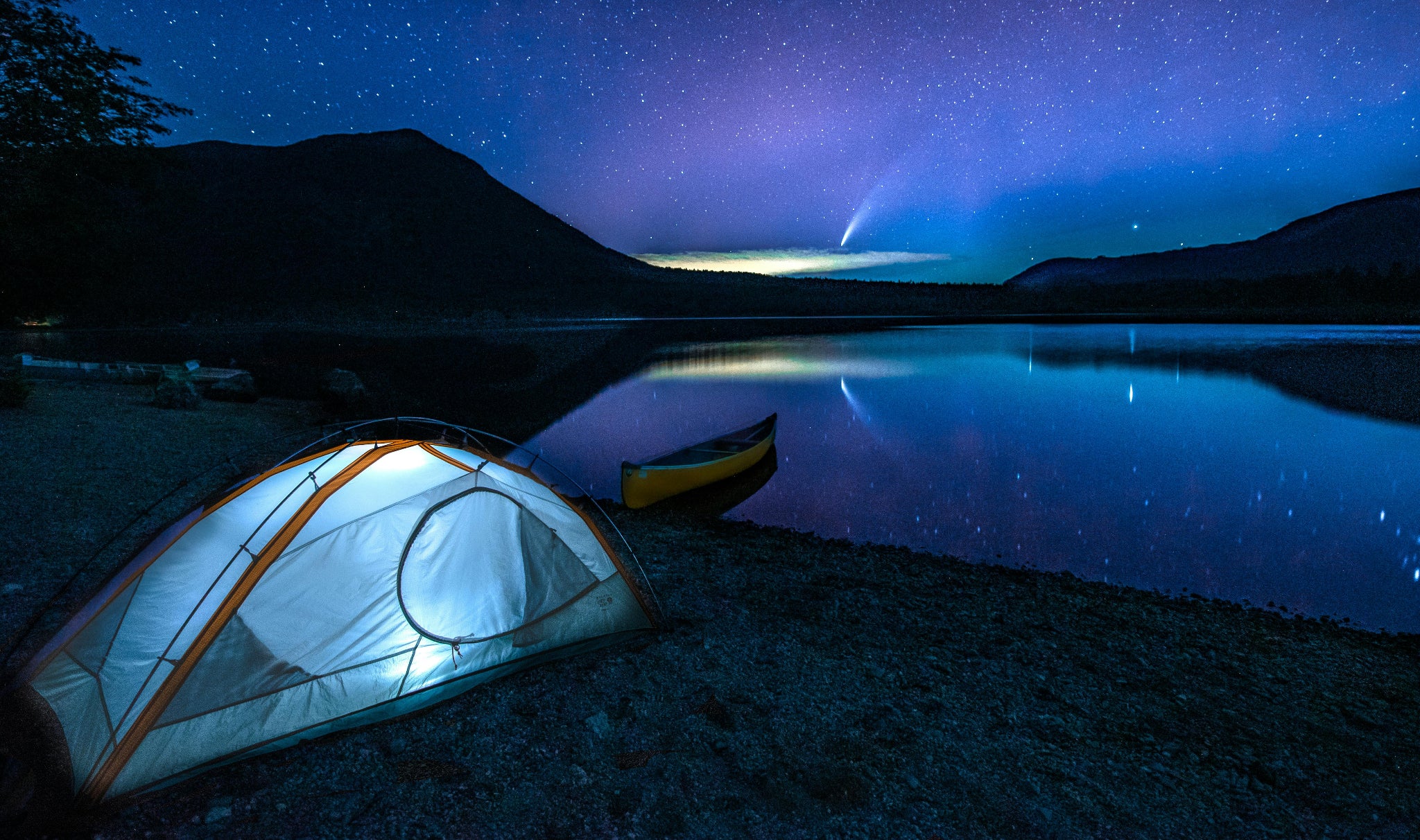 Tent illuminated by a HAVEN lantern next to a lake under a starry sky.