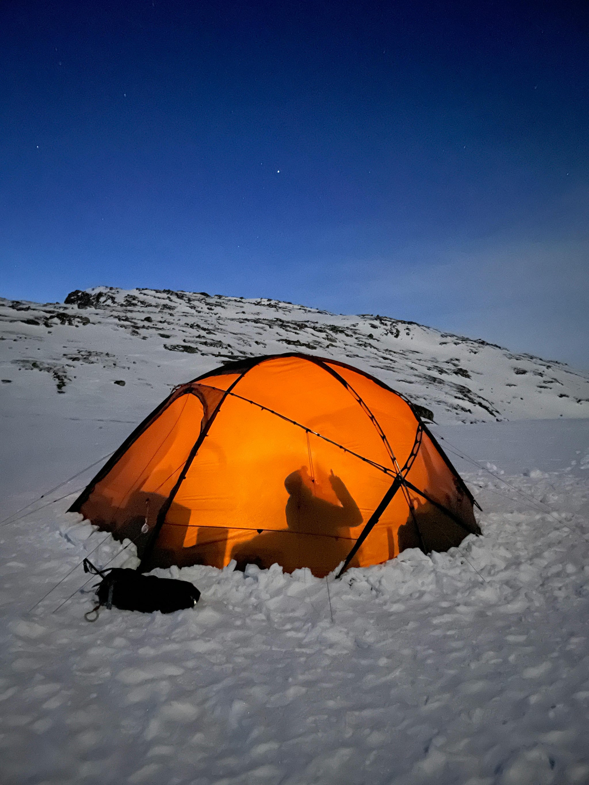 Orange camping tent illuminated by a HAVEN Lantern + power bank in a snowy landscape under a clear blue sky.