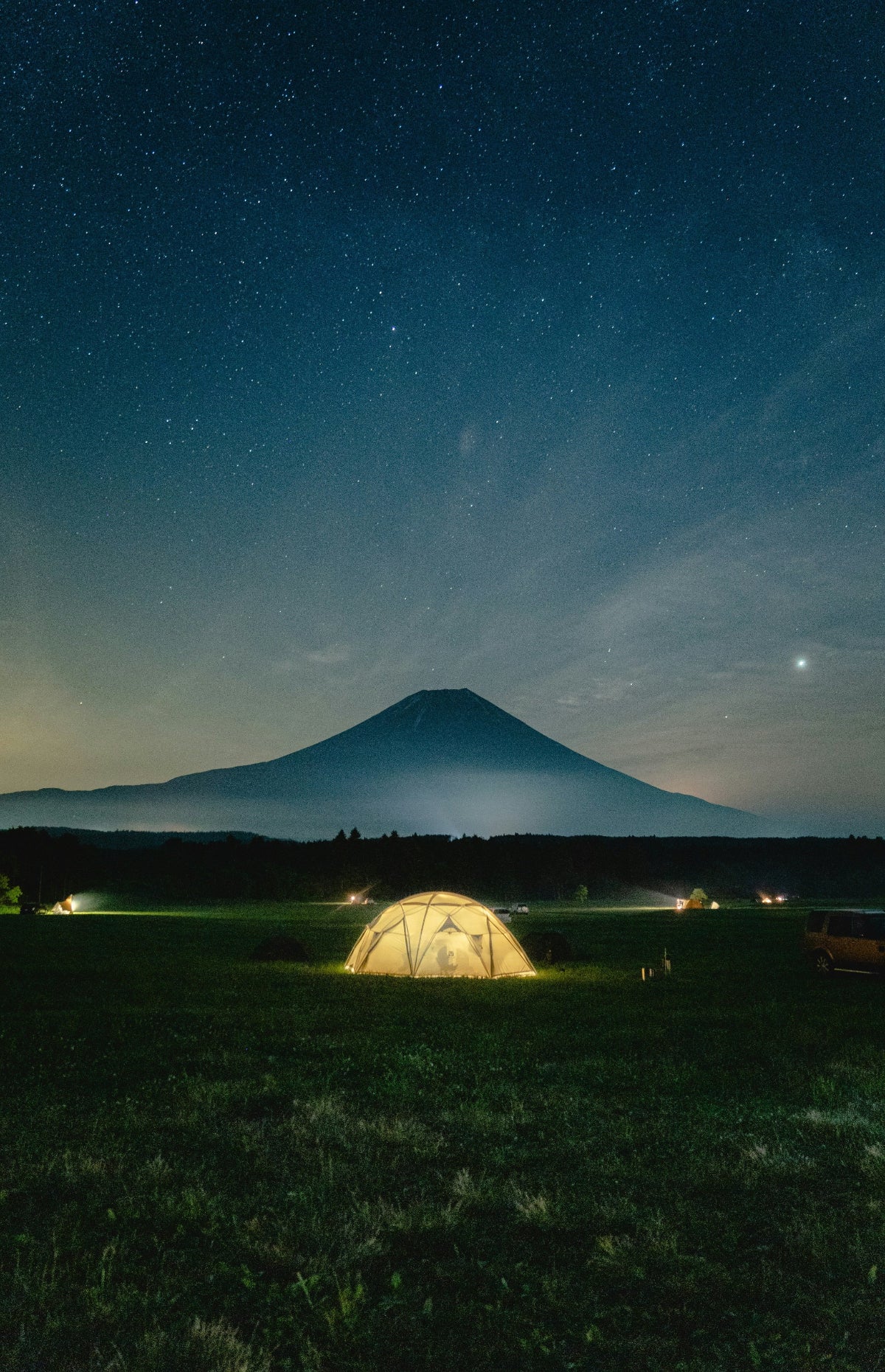 Camping tent illuminated by HAVEN solar portable lantern and power bank in a field with Mount Fuji and a starry night sky in the background.